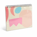 Cuaderno con espiral en el borde superior y portada geométrica rosa, azul y melocotón