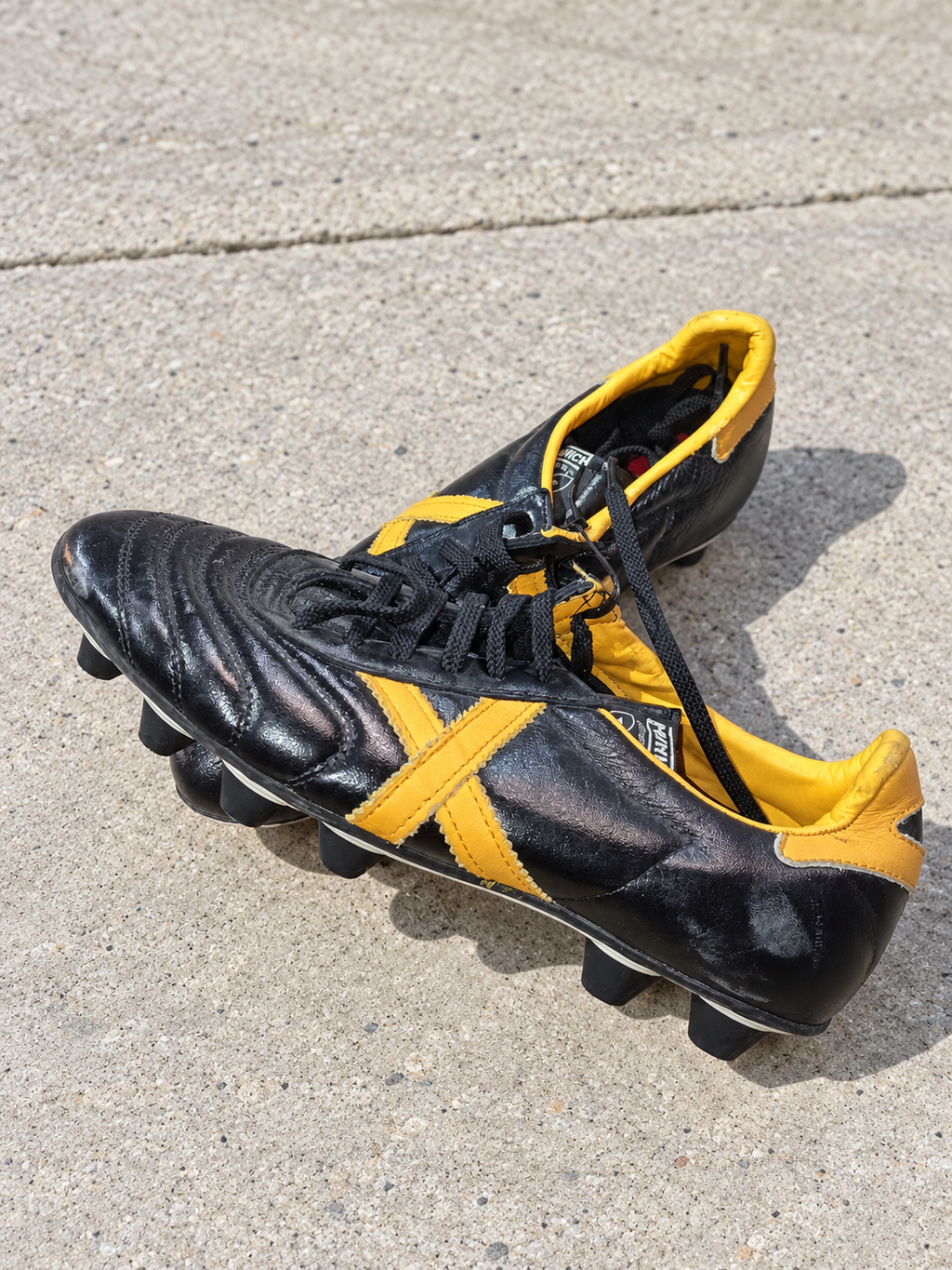 Botas fútbol Munich negras X dorada cuello amarillo talla 40 sobre pavimento