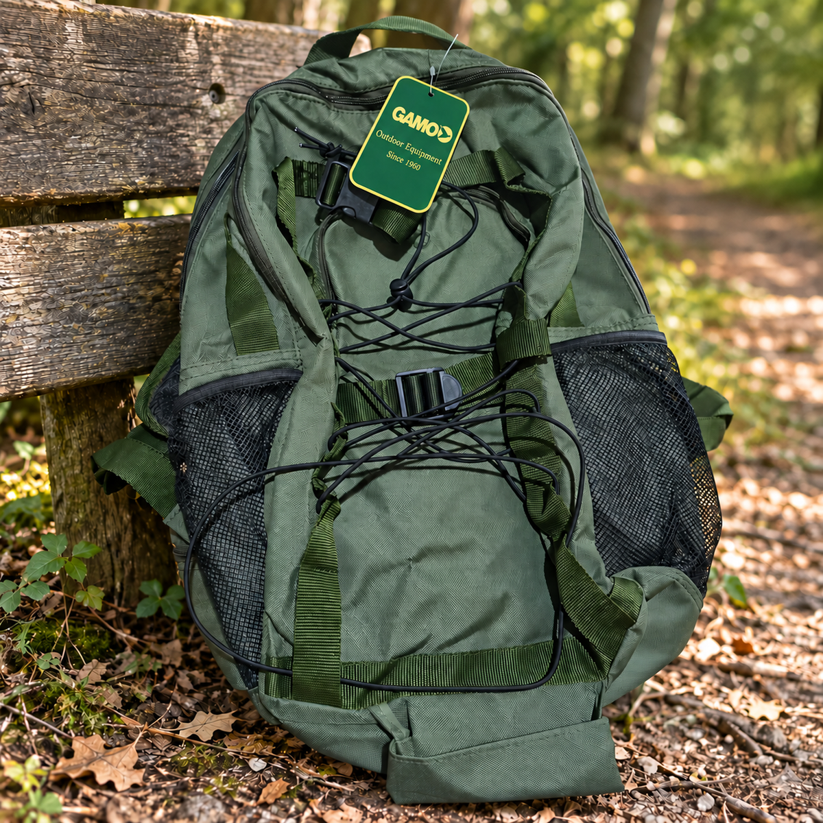 Mochila Gamo Rececho verde oliva vacía junto a un banco de madera en un sendero de bosque