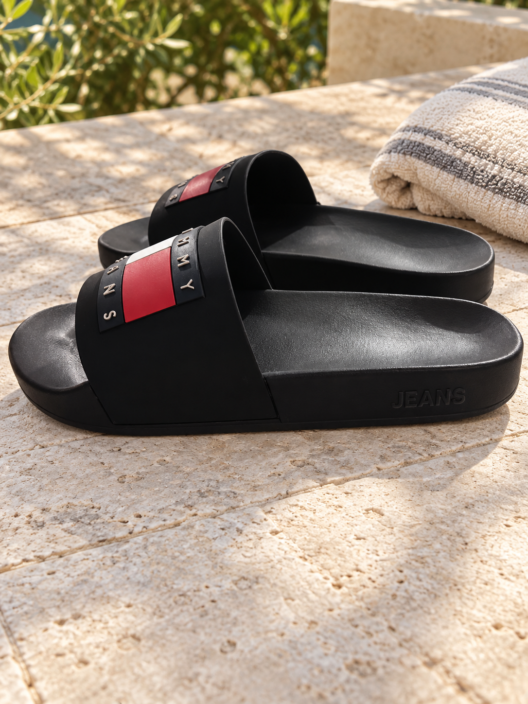 Chanclas Tommy Jeans negras sobre terraza junto a una toalla