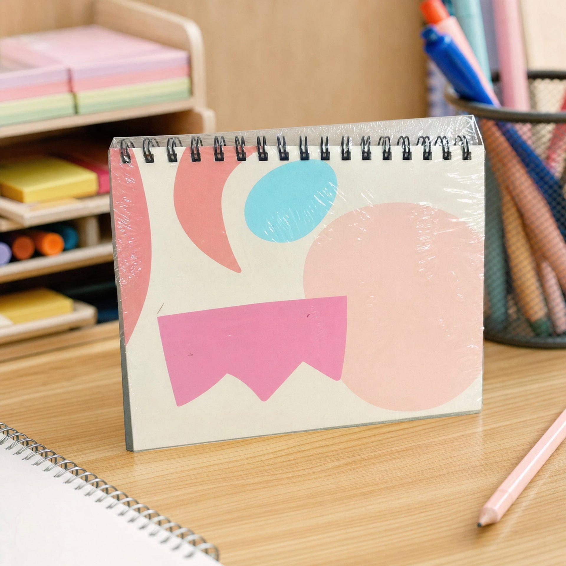 Cuaderno con espiral en el borde superior y portada geométrica rosa, azul y melocotón